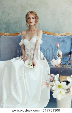 Bride In A Chic Long Dress Lying On The Sofa Couch. White Wedding Dress On The Bride's Body. Beautif