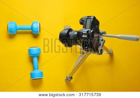 Fitness Blogger. Sport Concept. Plastic Dumbbells And A Camera On A Tripod On A Yellow Background. T