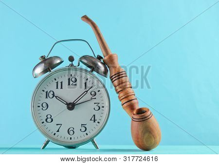 Retro Alarm Clock And Smoking Pipe Closeup On A Blue Background.