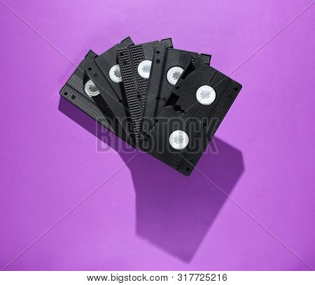 Stack Of Retro Video Cassettes On Purple Background. Top View