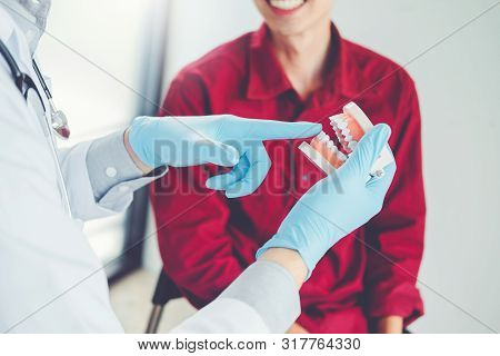 Dentist Talking To Smiling Male Patient And Showing Denture In Dental Office