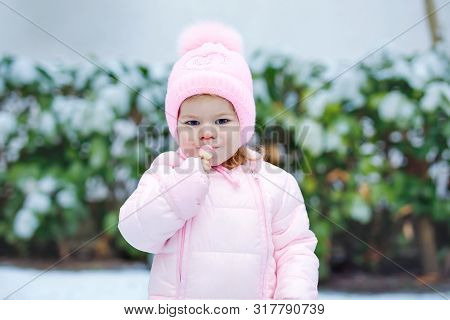 Portrait Of Little Toddler Girl Walking Outdoors In Winter. Cute Toddler Eating Sweet Lollypop Candy