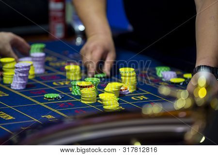 Roulette Table With Human Hands Putting Down Chips In Casino. Roulette Wheel In The Foreground. Gamb