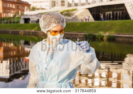 Female Ecologist Or Epidemiologist Visually Assesses The Quality Of Water In An Urban River, Looking