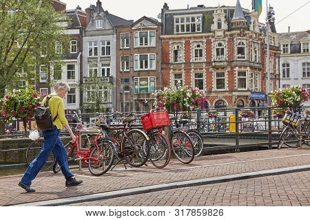 Man Crossing One Of The Many Bridges Over A Canal In Amsterdam Netherlands