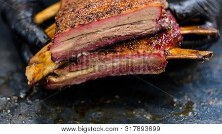 Culinary Master Class. Grilled Meat. Chef Hands In Black Cooking Gloves Holding Smoked Beef Ribs.