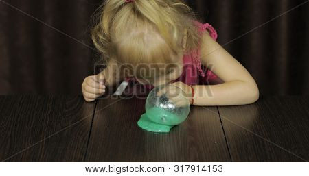 Child Having Fun Making Green Slime. Kid Playing With Hand Made Toy Slime. Funny Kid Girl. Blowing B
