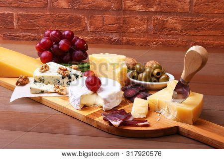 Assortment Of Cheese With Fruits, Grapes, Nuts And Cheese Knife On A Wooden Serving Tray.