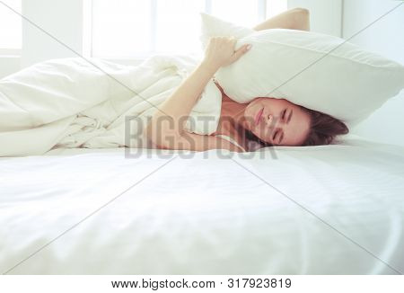 Young caucasian woman covering her head and ears with pillows.