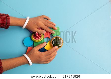 Top View Of Hand Of A Children Grabbing Colorful Wooden Building Blocks With Different Shapes For Pl