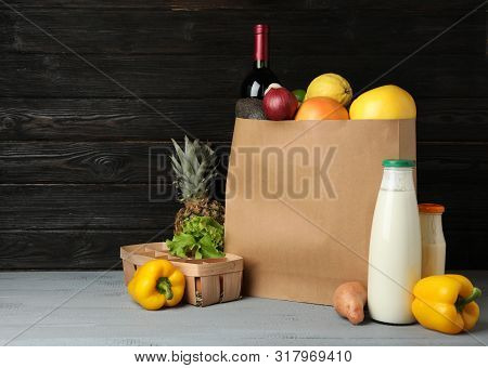 Paper Bag With Groceries On Wooden Table Against Dark Background. Space For Text