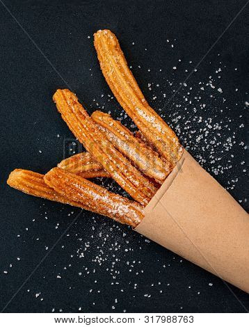Churro On A Black Background. Traditional Spanish Cusine. Churros In A Paper Bag With Copy Space. To