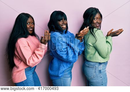 Three young african american friends wearing wool winter sweater pointing aside with hands open palms showing copy space, presenting advertisement smiling excited happy 