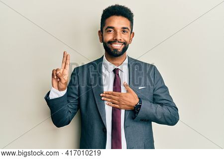 Handsome hispanic man with beard wearing business suit and tie smiling swearing with hand on chest and fingers up, making a loyalty promise oath 