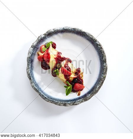 French Style Crepes - Cream Crepes with Berry and Fruit. Pancake Breakfast on white and blue plate isolated on white background. Mixed berry crepes garnished with mint and sweet sauce top view