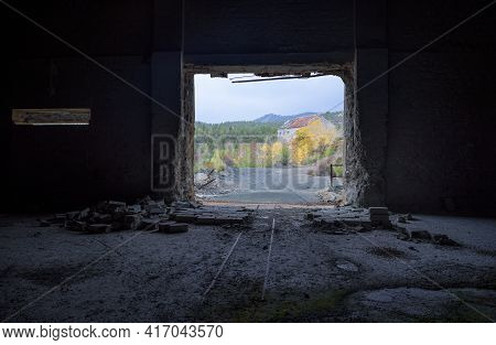 View Through The Door Of Abandoned Factory With Rails And Broken Brick Wall Inside And Autumn Landsc