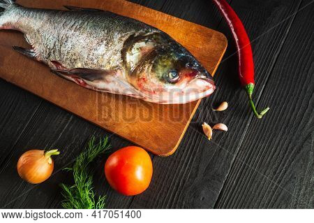 Hypophthalmichthys Or Bighead Carp On A Cutting Board With Vegetables Before Cooking. Raw Peeled Fis