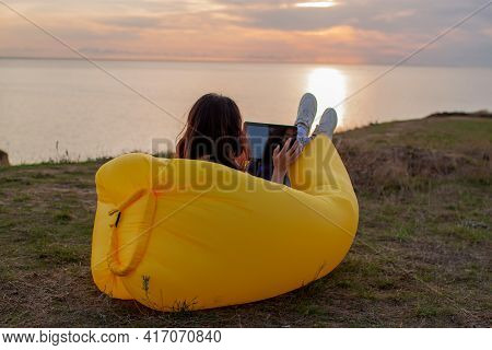 Asian Woman Lying On Inflatable Sofa Lamzac While Resting With Laptop At Sunset On The Mountain