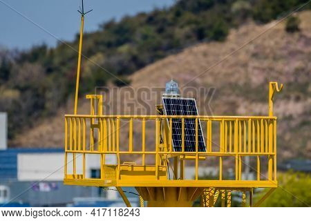 Small Solar Panel And Beacon On Top Of Yellow Lighthouse With Blurred Background.