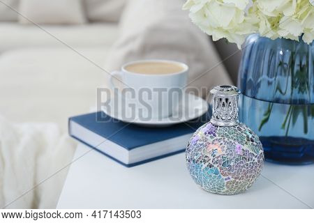 Stylish Catalytic Lamp With Cup Of Coffee, Book And Flower On White Table In Living Room. Cozy Inter
