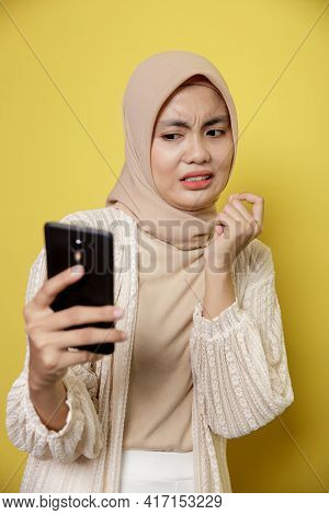 Young Woman Wearing Hijab With An Expression Disgusted While Looking Her Phone