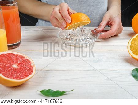 Young Woman Squeezes Orange Juice Using A Manual Glass Juicer.