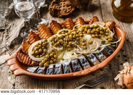 Fried Potatoes With Herring Fish Slices, Canned Green Peas And Onions In Plate On Wooden Rustic Tabl