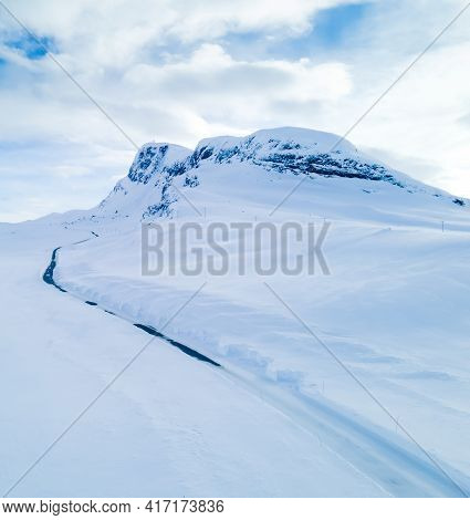 Lonely Road Winding Through A Snow Covered Mountain Landscape On A Cold Winters Day.