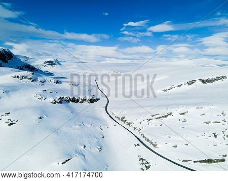 Lonely Road Winding Through A Snow Covered Mountain Landscape On A Cold Winters Day.