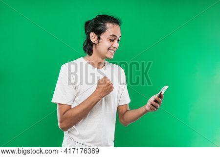 Portrait Asian Man Holding And Look Handphone With Happiness Expression While Raising One Hand And M
