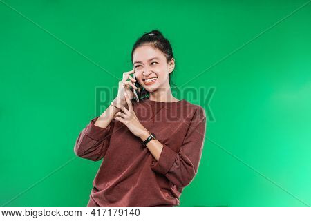 Beautiful Young Asian Woman Is Talking On The Phone Smiling Faintly With Someone While Looking Besid