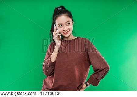 Beautiful Young Asian Woman Is Talking On The Phone Smiling Faintly With Someone While Looking Besid