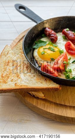 Fried Eggs In A Skillet With Hunting Sausages, Tomato, Parsley And Green Onions Vertical