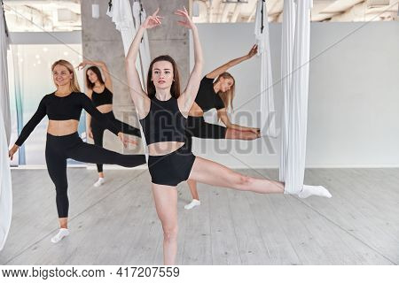 Group Of Female Are Doing Fly Yoga Exercises In Fitness Training White Gym Loft Classroom. Intense F