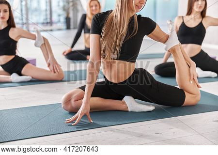 Group Of Female Athletes Are Stretching On The Yoga Mat. Intense Fitness Training Workout In Loft In
