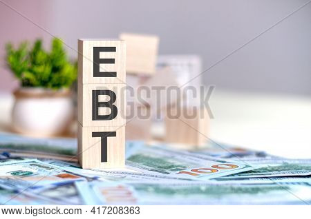 Wooden Cubes With The Letters Ebt Arranged In A Vertical Pyramid On Banknotes, Business Concept