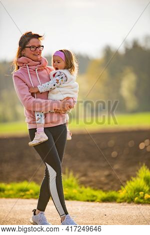 Mother And Child Walking On Countryside Road Between Agricultural Fields Towards Vilage From Forest.