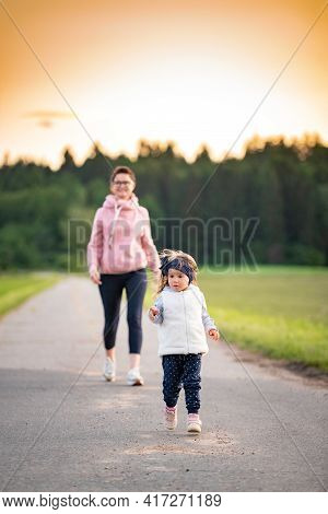 Mother And Child Walking On Countryside Road Between Agricultural Fields Towards Vilage From Forest.