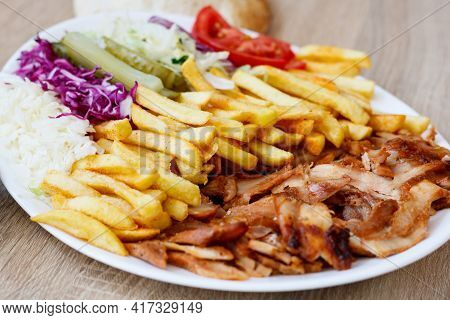 A Closeup Of Chicken Doner Kebab On A Plate With French Fries, Tomatoes, Onion, Pickles And Cabbage 