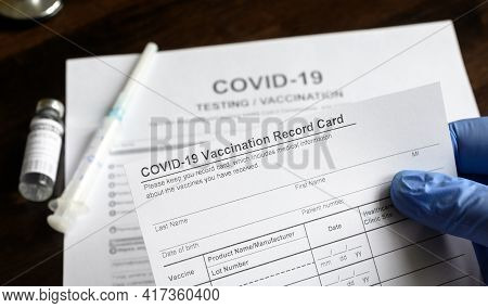 Covid-19 Vaccination Record Card In Doctor Hand, Coronavirus Test And Vaccine Medical Form On Desk I