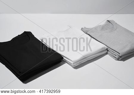 Three Folded Monochrome T Shirts Gray, Black And White Isolated Over Gray Background. Clothes, Fashi
