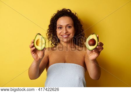 A Curly-haired Swarthy Woman, Wrapped In A Bath Towel Holding Avocado Halves And Showing Them To Cam