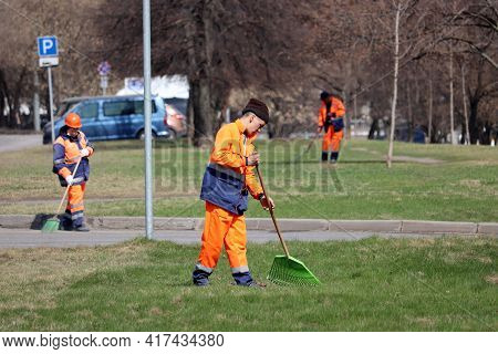 Moscow, Russia - April 2021: Janitors Clean The Lawns In Spring City. Street Sweepers With Rake, Wor