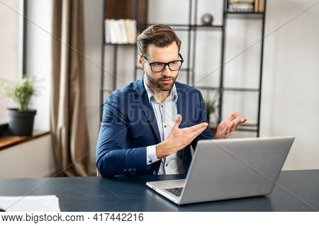 Slavic Stylish Man Talking At Laptop By Video Call, Focused Young Businessman In Eyeglasses Involved