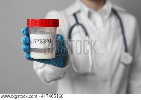 Doctor Holding Container With Sperm On Grey Background, Closeup. Space For Text