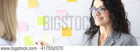 Business Woman Showing Colleague With Ballpoint Pen Stickers On Chalkboard