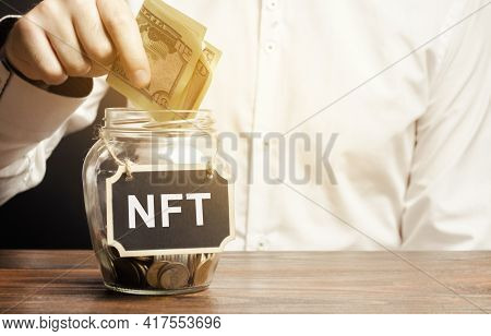 Hand Puts Dollar Bills In Glass Jar With The Word Nft. Non-fungible Token. Digitally Represented Pro