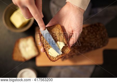 food cooking, baking and people concept - female baker spreading butter on slice of homemade bread