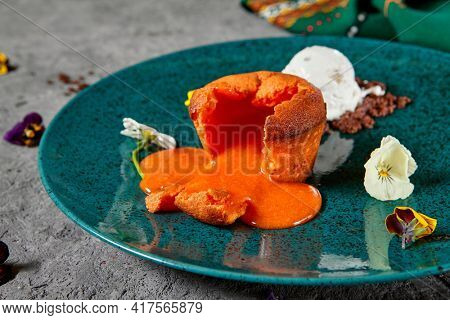 Carrot Fondant Cake with Ice Cream. Carrot Cake with liquid center served hot with ice cream. Dark green restaurant dish on textured gray table