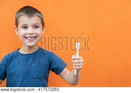 Boy Without Milk Upper Tooth In Blue T-shirt Holds Toothbrush In His Mouth On The Orange Background.